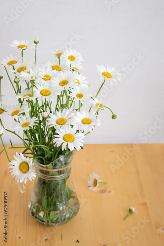 Fototapeta Naklejka Na Ścianę i Meble -  A bouquet of daisies stands in a glass jug on a wooden table.