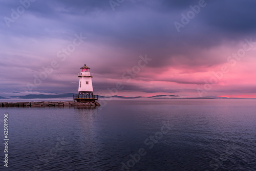 The Burlington Lighthouse before the storm under a cloudy, colorful sky at sunset. The sky is threatening. On the horizon, we can see that the clouds are low.