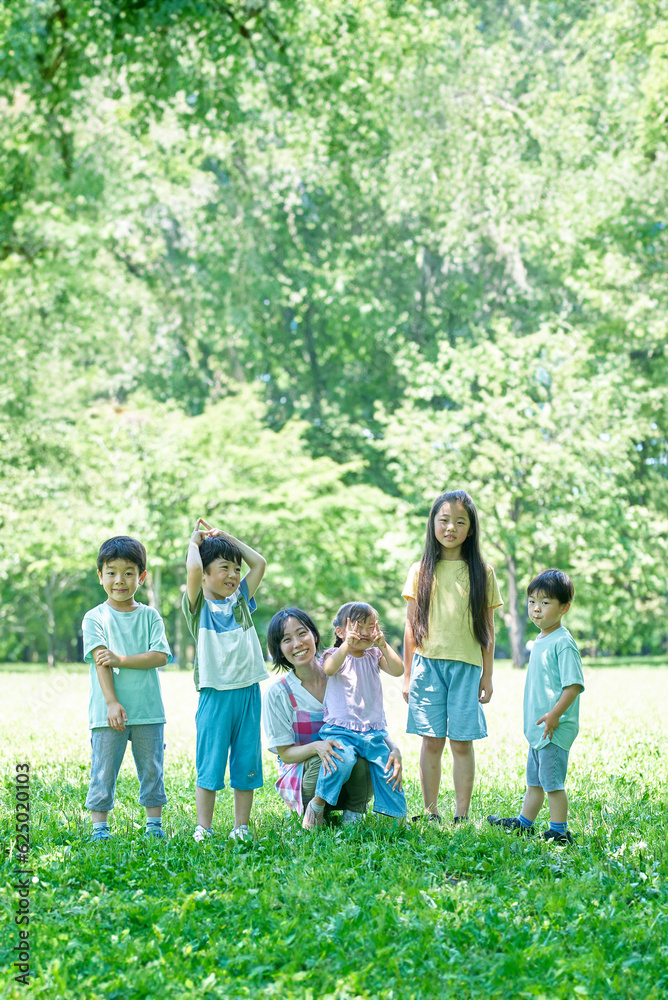 Obraz premium 緑地で、一列に並ぶ子どもたちと女性