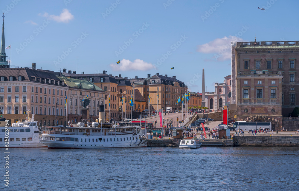 The sloop Slottsbacken in the old town Gamla Stan, Swedish flags, pier with boats, a sunny summer day in Stockholm