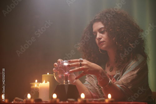 Canvas Print Pensive sorceress gazing into crystal ball when sitting at table with burning ca