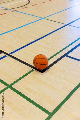 Single basketball lying on basketball court with colourful dividing lines at gym, copy space