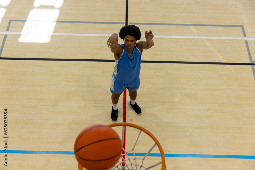 Naklejka premium Biracial male basketball player wearing blue sports clothes and shooting basketball at gym