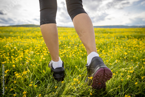 Woman runner legs on flowers trail on high altitude grassland