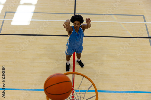 Biracial male basketball player wearing blue sports clothes and shooting basketball at gym © wavebreak3
