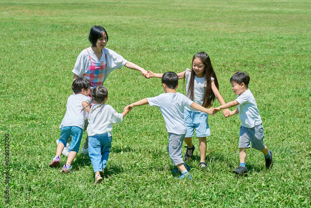 草原で輪になって遊ぶ子どもたちと女性 草原で輪になって遊ぶ子どもたちと女性
