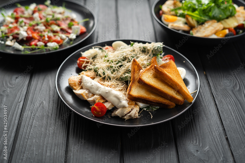 Food. Set of dishes, Caesar salad, baked pepper with cheese and vegan food on the table on a black wooden background Food. Set of dishes, Caesar salad, baked pepper with cheese and vegan food on the table on a black wooden background