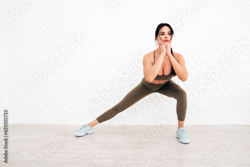 Fitness woman in sports clothing. Sexy young beautiful model with perfect body wearing sportswear. Female making exercises at home in white interior. Stretching out before training. Makes lunges