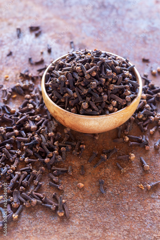 dried cloves spice in wooden bowl on rusty table background. dried cloves spice in wooden bowl on rusty table background.