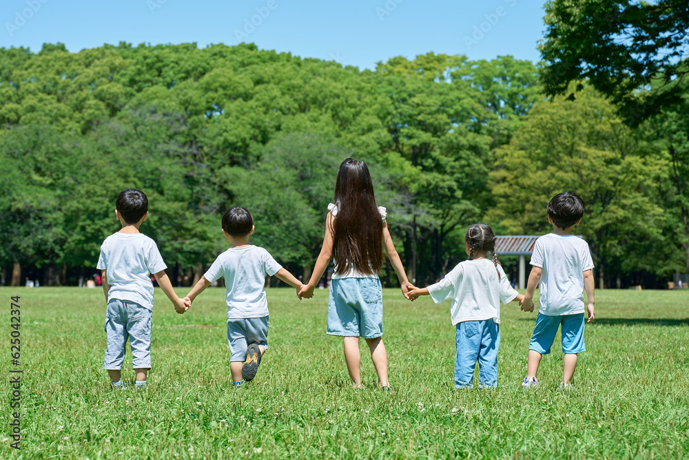Obraz premium 草原で手を繋いで並ぶ子どもたちの後ろ姿