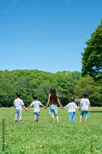 草原で手を繋いで並ぶ子どもたちの後ろ姿