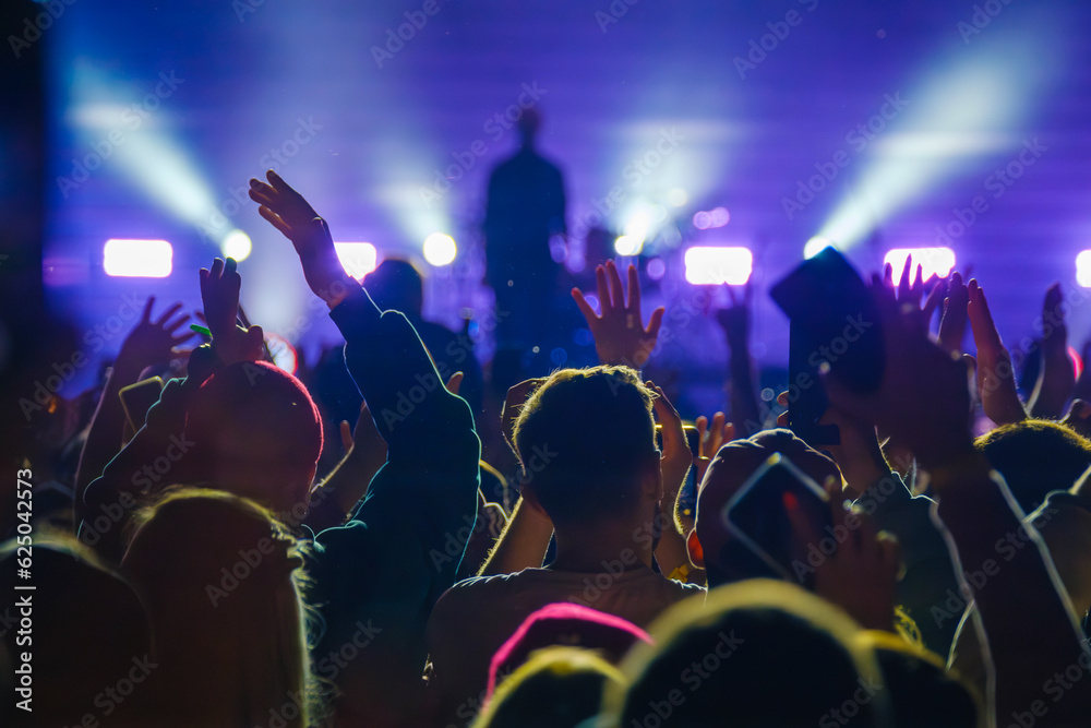 Unrecognizable people showing raised hand gesture to artist on stage in live concert