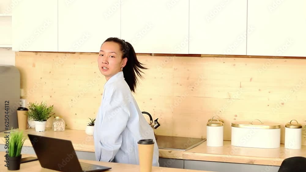 Asian girl works freelance remotely at home in the kitchen sitting at a laptop Asian girl works freelance remotely at home in the kitchen sitting at a laptop