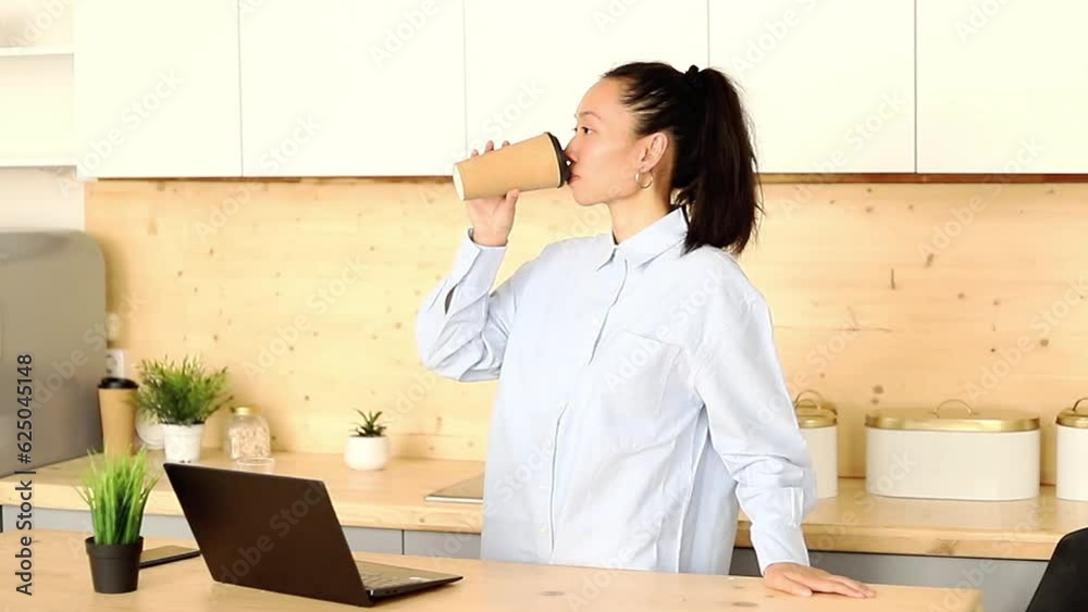 Asian girl works freelance remotely at home in the kitchen sitting at a laptop Asian girl works freelance remotely at home in the kitchen sitting at a laptop