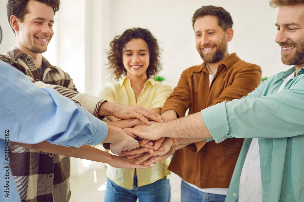 Obraz premium Portrait of a happy smiling young people friends or a group of students gathered together and putting their arms in a stack standing at home. The concept of friendship, unity and teamwork.