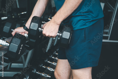 Handsome male athlete with dumbbell exercise in fitness gym, during strength training body at gym, happy in fitness to exercise, concept burning excess body,with exercises that the trainer plans