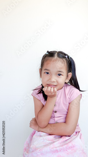 Cute child holding her hand on her chin and smiling at camera. Isolated on light color background.