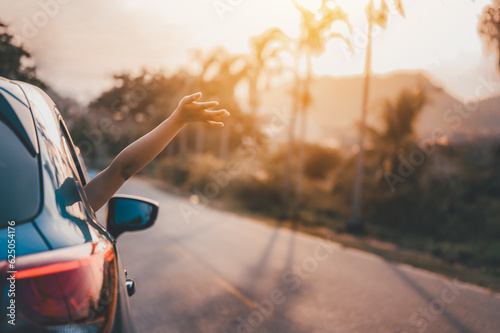 Road trip, Travel and vacation concepts. Happy woman hand out window car blue and driving on country road into the sunset. Happy woman with sunlight.