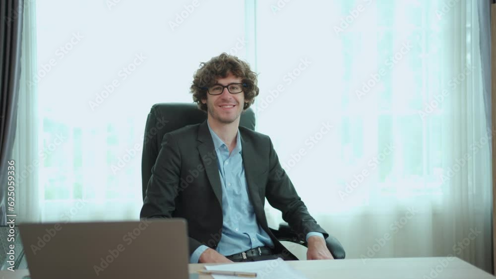 Smart - good looking senior male managing director working in the office on laptop computer and documents. Businessman or CEO turning around the chair and looking at camera. Smart - good looking senior male managing director working in the office on laptop computer and documents. Businessman or CEO turning around the chair and looking at camera.