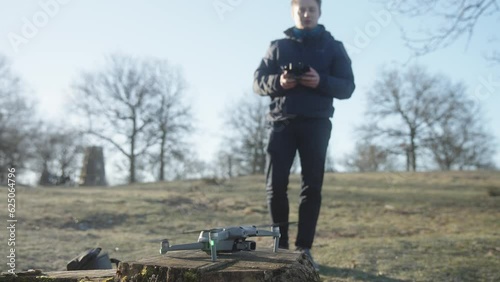 Young male dronepilot setting up a drone and lift off into the air with remote control for flying on a drone operation in nature on a cold spring morning photo