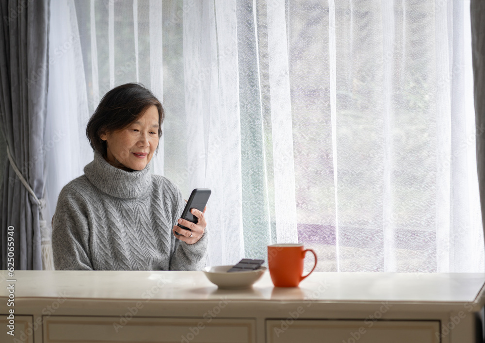 Senior woman smiling and reading smartphone. A coffee cup and dark chocolate on white table.