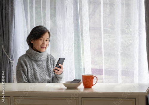 Obraz na płótnie Senior woman smiling and reading smartphone. A coffee cup and dark chocolate on white table. w salonie