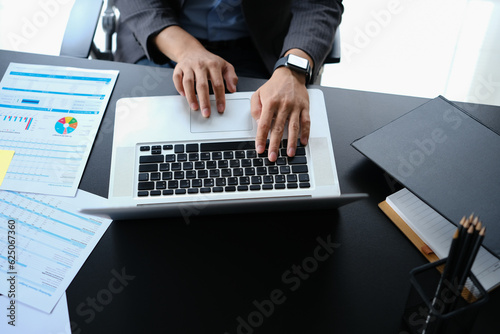 Above view of businessman hands typing on laptop, working with financial graph, statistics document at workplace