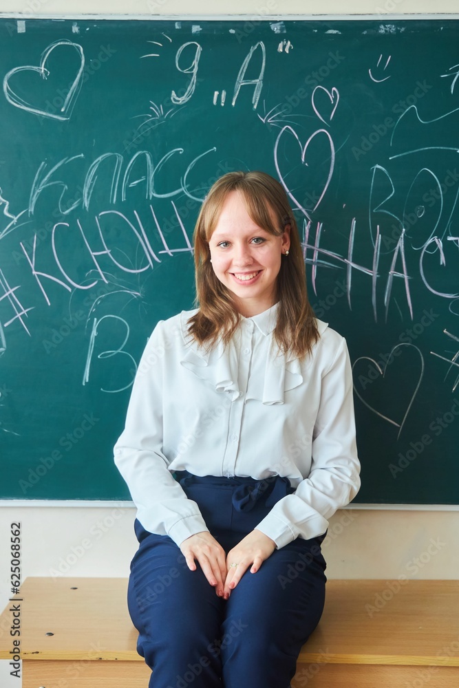 A schoolgirl girl is sitting on a desk at the blackboard. High school graduates.