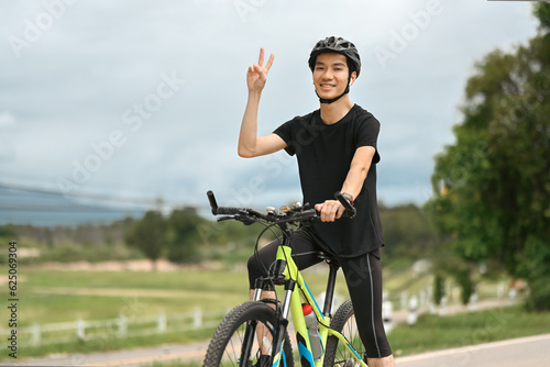 Happy asian man dressed in casual clothes and helmet riding a bicycle along the bike path in summer park