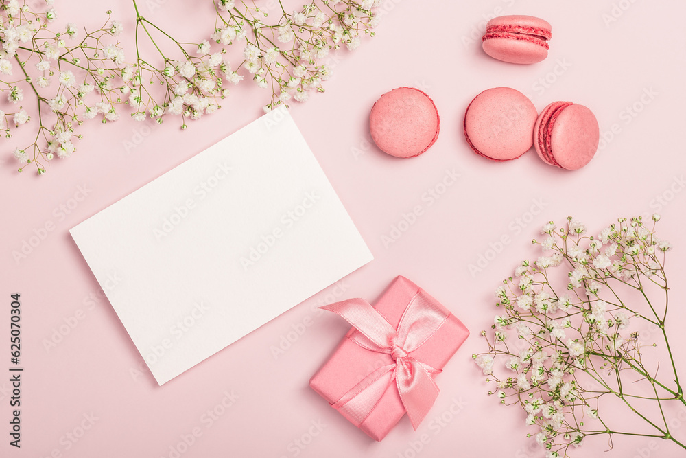 Flat lay composition with empty blank, macaroons, gift box and gypsophila on pink background. Stylish women's workplace. Greeting card. Invitation