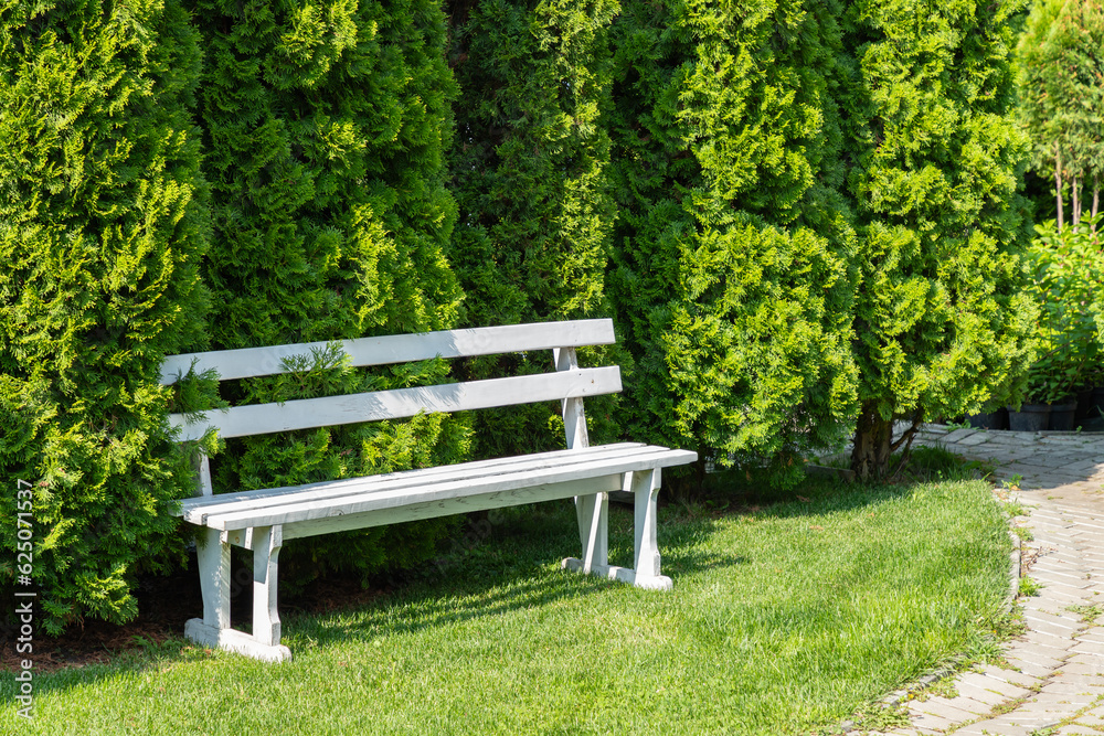 Scenic view of a peaceful green garden. White bench in garden. Scenic view of a peaceful green garden. White bench in garden.