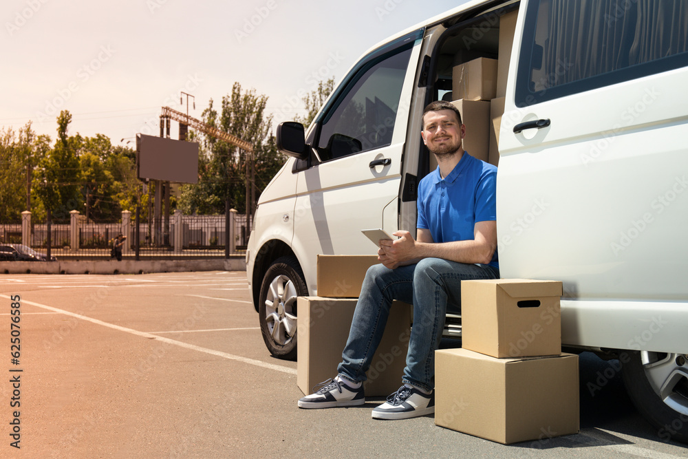 A courier with a tablet in his hands near a car with boxes A courier with a tablet in his hands near a car with boxes