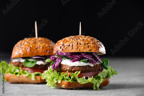 Two vegan burger with vegetables and sauce on dark background. Healthy food concept.