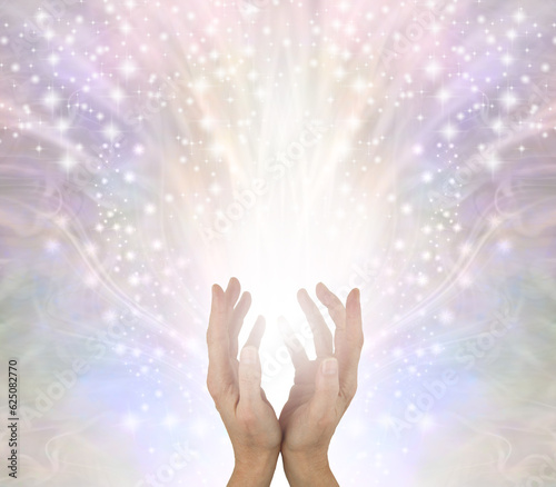 Sending you beautiful high vibe  healing energy - female cupped hands with white light and  sparkles flowing up and out on a pale wispy energy field background with copy space 
