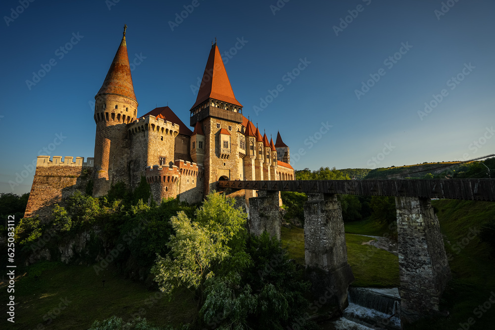 Corvin (Hunyad) Castle in Hunedoara during the sunset. Wide angle photo this amazing medieval castle landmark in Romania with the main river and bridge in foreground.