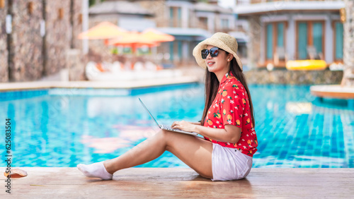 Traveler woman in hat sit on modern luxury pool using laptop computer, Asia business people on vacation at private resort, Attraction leisure tourist travel and work in Phuket Thailand summer holiday