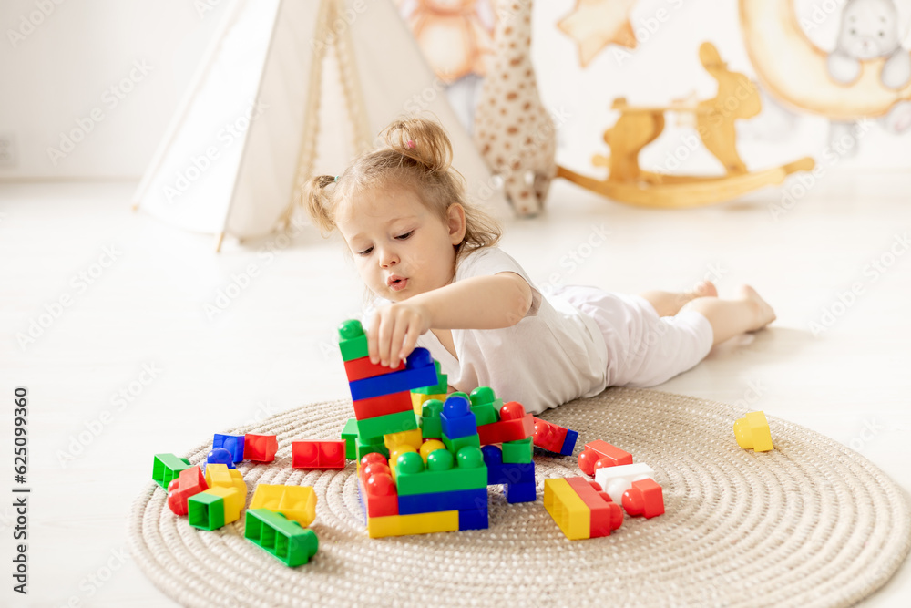 blonde girl plays in the children's room with colored cubes, stands a tower, children's leisure, kindergarten blonde girl plays in the children's room with colored cubes, stands a tower, children's leisure, kindergarten