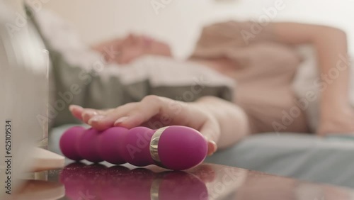 Young Caucasian woman taking pink vibrator from her nightstand while relaxing in bed alone in morning photo