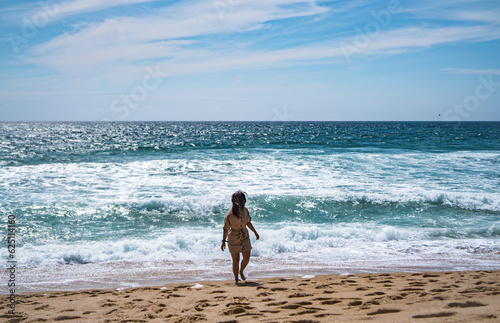 A girl is walking and looking back next to the calm ocean in Nazare  summertime  Portugal