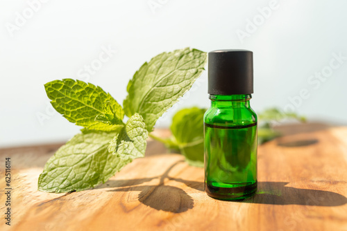 Fototapeta Naklejka Na Ścianę i Meble -  Green bottle of essential oils. natural cosmetics for skin care. A bottle and fresh mint on a wooden table. Taking care of health and beauty.