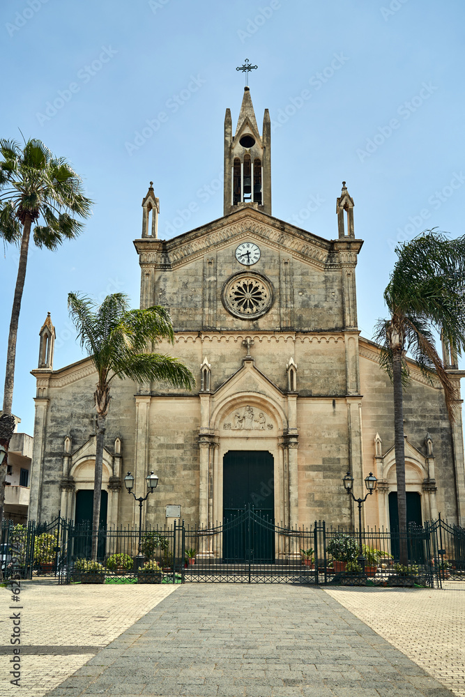 Baroque facade of a historic church with a clock and a bell tower on the island of Sicily