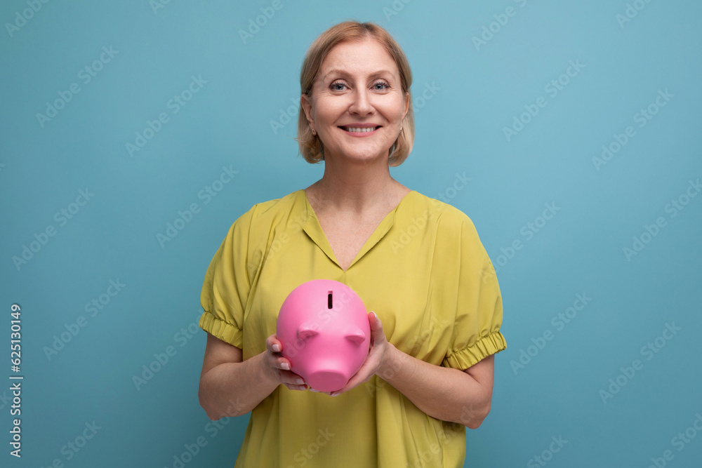 successful blonde mature woman keeps money in a piggy bank and thinks where to invest it successful blonde mature woman keeps money in a piggy bank and thinks where to invest it