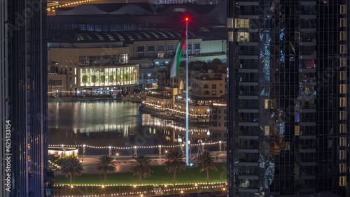 Aerial view of Dubai Fountain in downtown with palms in park next to shopping mall and souq night to day timelapse, UAE