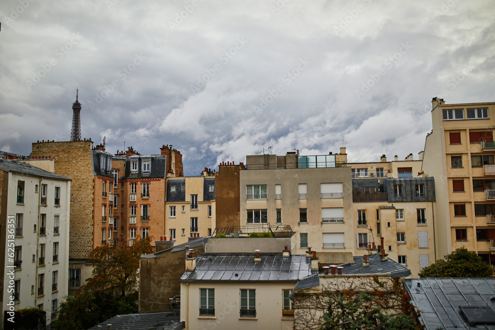 View of the Eiffel tower with dramatic cloudscape over the roofs of residential buildings in Paris