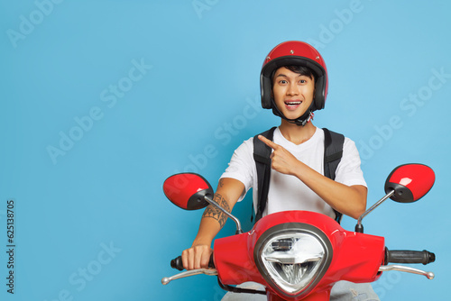 Tela Delivery man in red helmet on red scooter in blue studio, one hand on handle bar