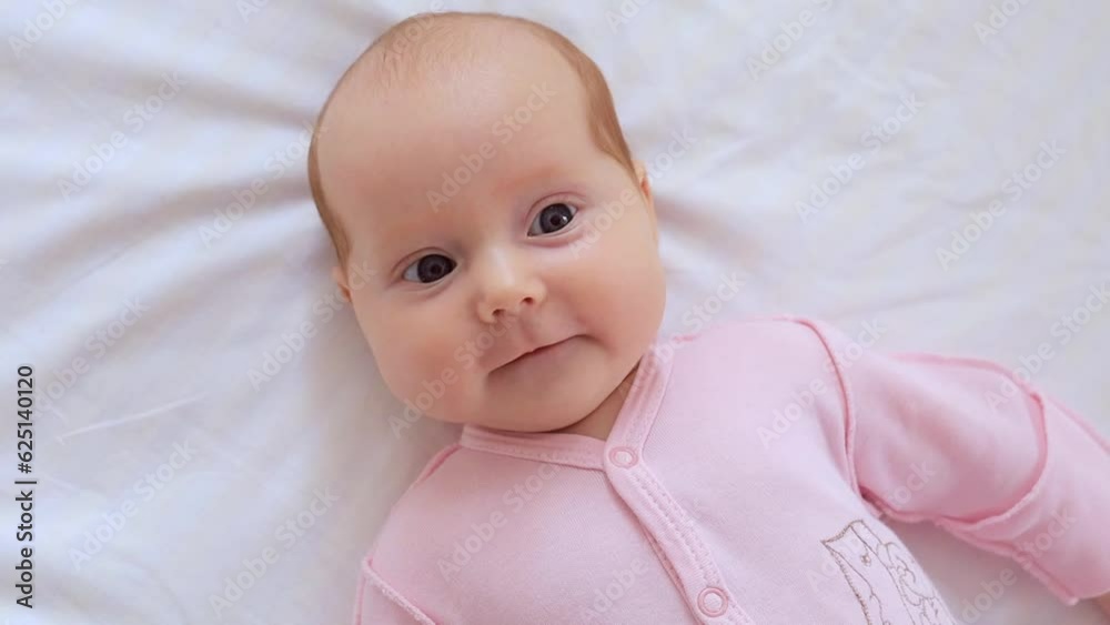 close-up portrait of a small newborn baby girl with blue eyes lies on a white cotton bed at home and smiles close-up portrait of a small newborn baby girl with blue eyes lies on a white cotton bed at home and smiles