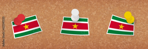 Suriname flag pinned in cork board, three versions of Suriname flag.