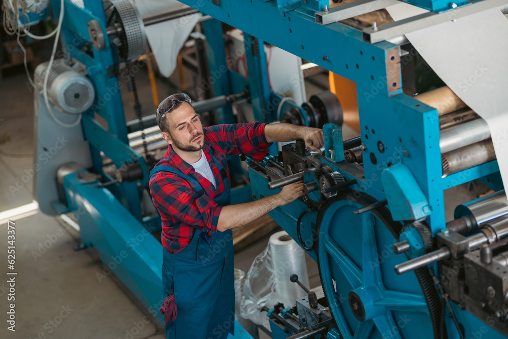 The young craftsman works on a large printing machine in the company. The young craftsman works on a large printing machine in the company.