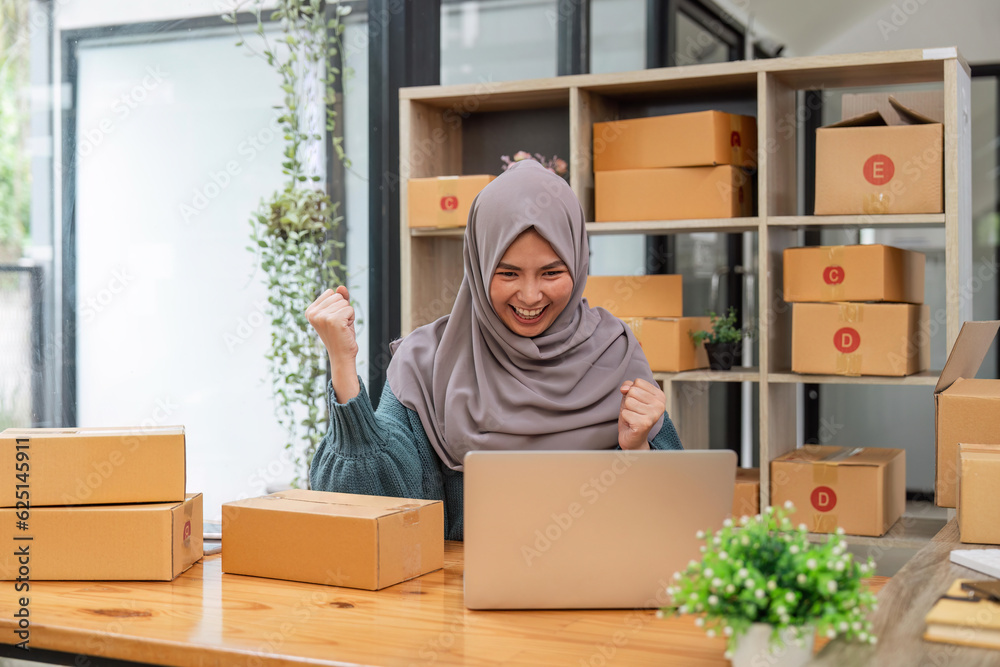 Young attractive beautiful Muslim female entrepreneur, SME business owner celebrating an online selling win after a new order from the customer Young attractive beautiful Muslim female entrepreneur, SME business owner celebrating an online selling win after a new order from the customer