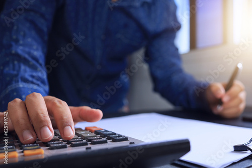 Businessman hand calculating statistical values including profit and loss by using calculator on desk by window with good light to create good working atmosphere.